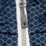 Close-up of a blue quilted fabric with a white zipper, featuring a gray zipper pull embossed with the Maserati trident logo.