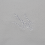 Close-up of the Maserati trident logo embroidered in white thread on light fabric.