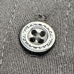 Close-up of a metallic button engraved with the Maserati name, stitched onto dark fabric.